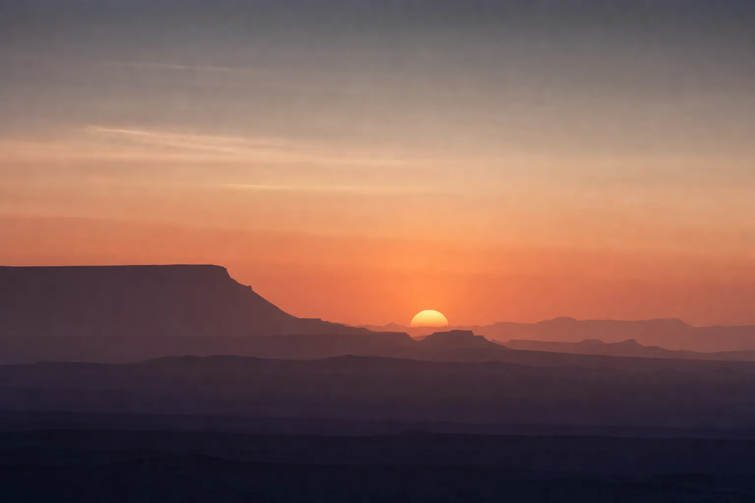 A low desert horizon at late afternoon with the sun sitting as a half-disc behind layered mesas — an illustrative scene, not a photograph of Katie Jordan.